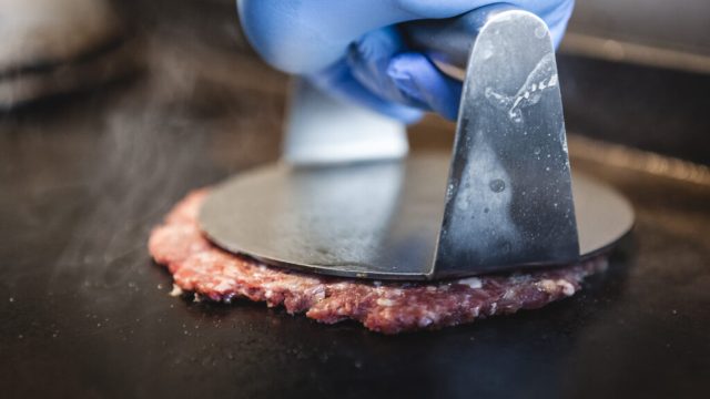 A JEM smash burger patty being pressed on the flat-top grill